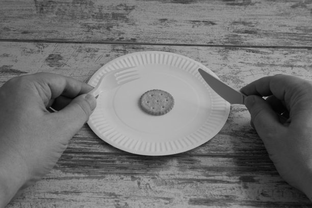 手里拿着刀叉放着一盘饼干黑白照片，食品价格上涨，低热量饮食，食物短缺，分量小图片下载