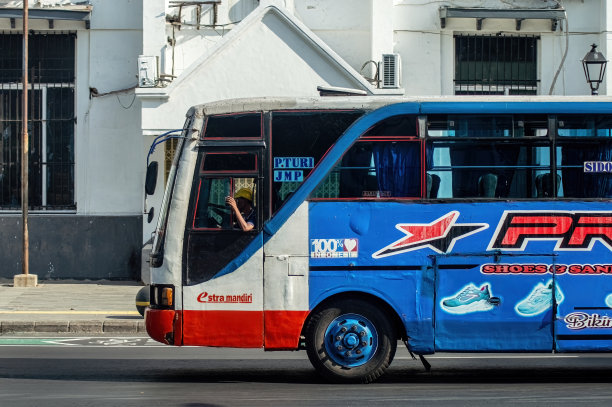 2024年6月20日，印度尼西亚泗水，一辆在门口站着一名乘务员的情况下快速穿过城市的旧公交车看起来很危险。图片下载