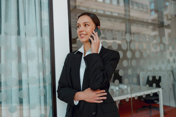一个在办公大楼里的女商人，用她的智能手机说话，显示出专注和能力图片下载
