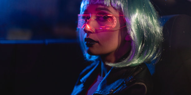 在汽车中使用虚拟现实眼镜的女性肖像。霓虹灯概念摄影，未来主义照片与车内彩色照明。女孩和神经网络，人和交流技术。图片下载