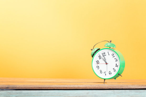 复古绿色闹钟，5分钟到12点响在木制桌子前黄色背景。复古的老式滤镜照片图片下载