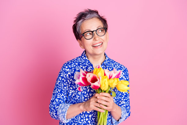 漂亮的人的照片，白色灰色的发型，穿着印花衬衫，拿着郁金香，看着销售，空白的空间孤立在粉红色的背景上图片下载