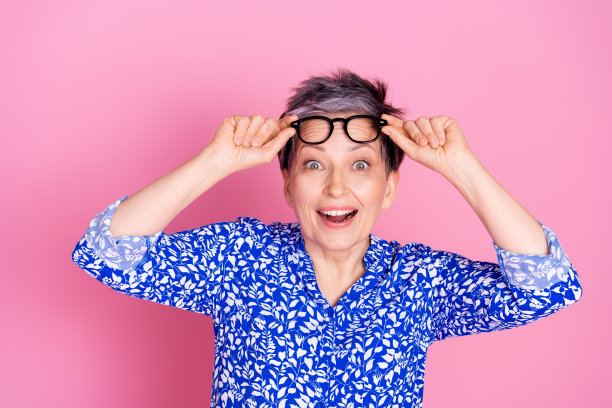 印象深刻的老人的照片，白发，穿着印花衬衫，触摸眼镜，惊讶地凝视着孤立的粉红色背景图片下载