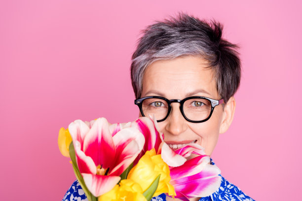 照片中，开朗的老人留着灰白的发型，穿着印花衬衫，在粉红色的背景上散发着五彩缤纷的郁金香的味道图片下载