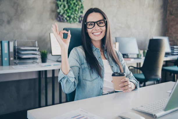 快乐迷人的女士助理的照片穿牛仔裤衬衫显示ok喝饮料在室内车间工作站阁楼图片下载