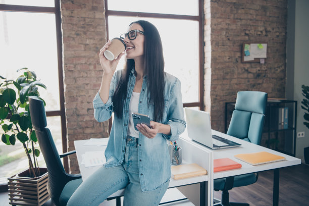 照片肖像漂亮的年轻女孩喝咖啡装置穿时髦的牛仔服装现代职场成功的企业主家庭办公室图片下载
