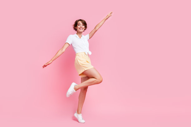 全身长度的照片，无忧无虑的女人飞翅膀的手有乐趣在户外穿着时尚的衣服孤立的粉红色背景图片下载