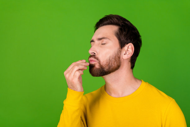 照片中，一个心情很好的男人，留着时髦的胡子，穿着黄色衬衫，在鲜艳的绿色背景上品尝美味的食物图片下载