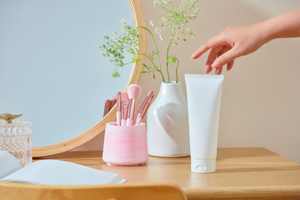 广告照片上，一个白色的没有品牌的化妆管，放在化妆台上，一个美丽的女人的手正在触摸它。除了用化妆用具和花瓶装饰图片下载