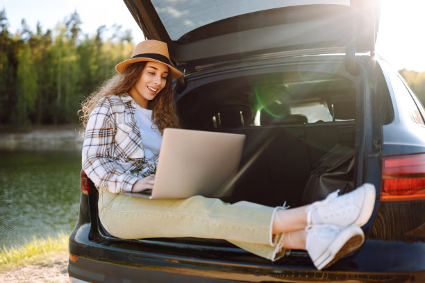年轻女子坐在汽车后备箱里使用笔记本电脑。图片下载
