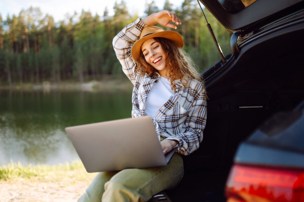 年轻女子坐在汽车后备箱里使用笔记本电脑。图片下载