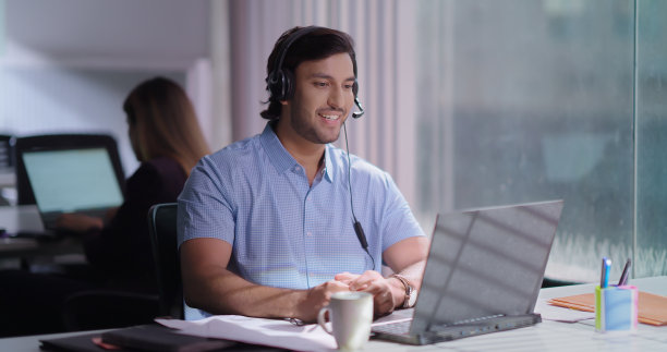 印度快乐的年轻人z世代男人男人坐椅子戴耳机做工作在线聊天远程视频呼叫中心工作。员工经理员工使用笔记本电脑看屏幕远程提供客户支持服务对话室内办公场所图片下载
