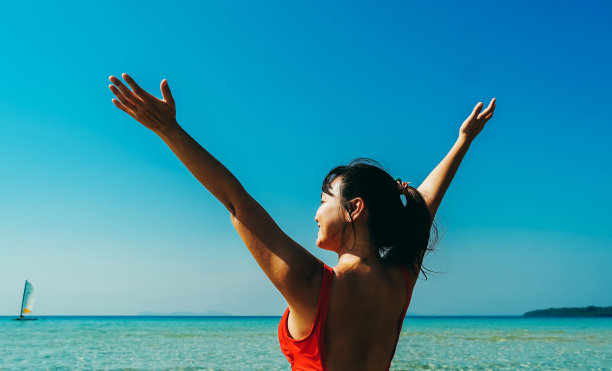 美丽的女人在海浪后视图。在泰国的古德岛，穿着比基尼的女子抬起手臂，开心地欣赏着令人惊叹的景色。夏季度假的图片完美的热带海滩的概念。图片下载