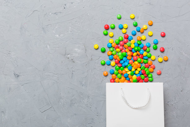 购物纸礼品袋在角落里充满了各种传统糖果落在彩色背景与复制空间。快乐假期销售概念图片下载