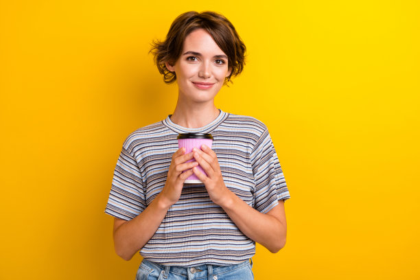 照片中可爱的漂亮女孩穿着时髦的衣服，拿着甜美的热芳香饮料，孤立在黄色的背景上图片下载