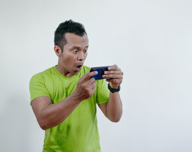 一名亚洲男子带着震惊的表情玩手机游戏。图片下载