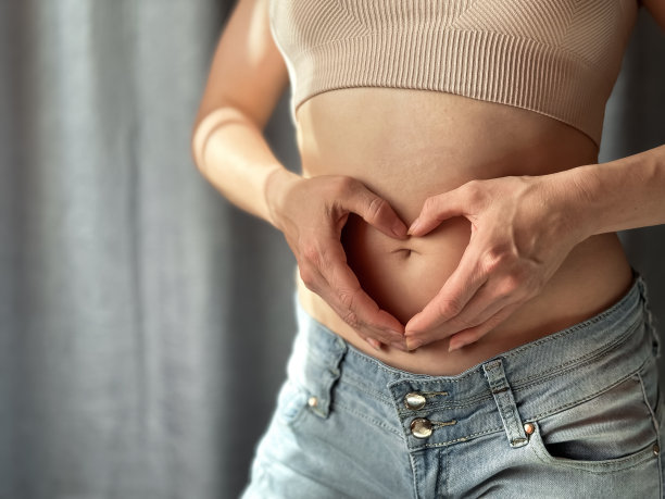 特写:苗条的女人穿着短上衣和牛仔裤，双手放在露出的肚子上，形成心形。身体积极，自爱和健康意识的概念。生活照片。图片下载