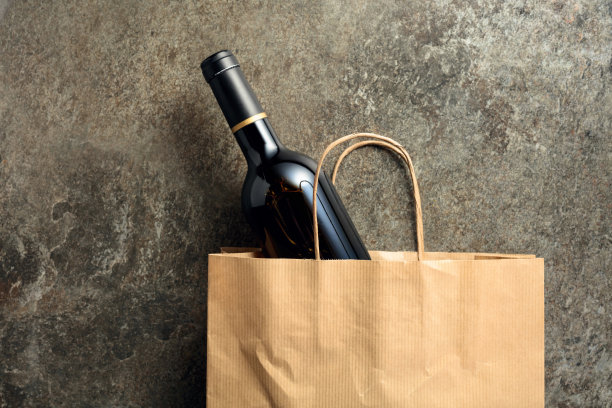 纸购物袋与一瓶红酒在一个古老的石头背景。图片下载