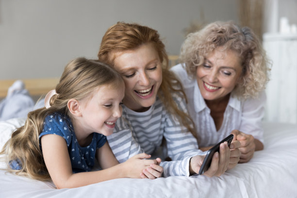 小女孩的妈妈和奶奶在床上玩智能手机图片下载