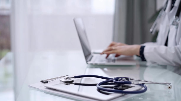 玻璃桌上放着听诊器和医用写字板，女医生正在用笔记本电脑工作。医学与药学概念图片下载