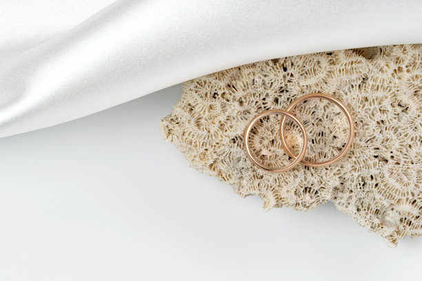结婚戒指躺在一个复杂的珊瑚，白色丝绸织物旁边图片下载