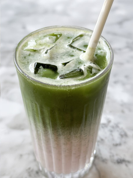 喝一杯冰抹茶拿铁的特写图片，两种色调的绿色和白色的无酒精饮料与吸管，冰块和牛奶上面有绿色抹茶，白色大理石桌面背景，抬高的视图，重点在前景图片下载