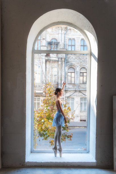 年轻的芭蕾舞女演员站着，背对着镜头，被一扇拱形的窗户框住图片下载