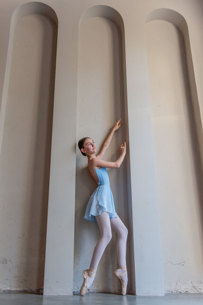 优雅的年轻芭蕾舞女演员身穿蓝色服装，踮着脚尖，轻轻地举起双臂，在阳光下弓着身子图片下载