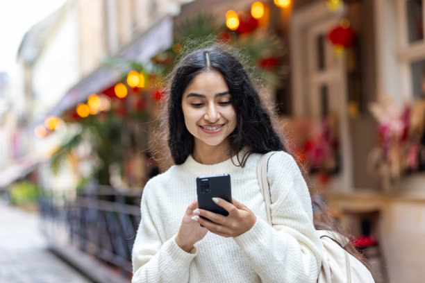 一个快乐微笑的印度女孩用手机的特写照片，她背着背包在城市外面散步图片下载