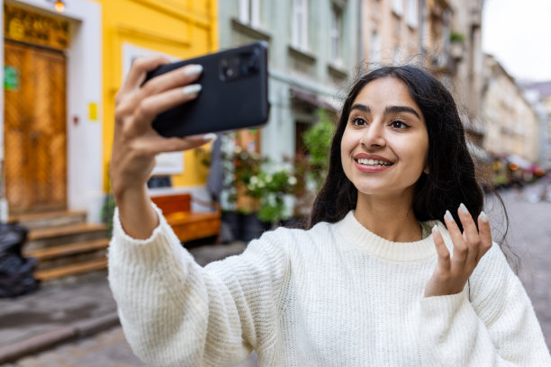 一个微笑的年轻印度女孩走在城市街道上的特写照片，她一边自拍一边打电话图片下载