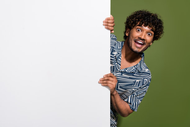 年轻震惊的墨西哥男子的照片，波浪的头发隐藏在白色横幅空的空间，为您的广告孤立的卡其色背景图片下载