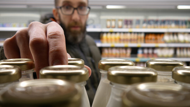 超市里许多玻璃瓶奶制品的特写镜头，一位男顾客拿了一个图片下载