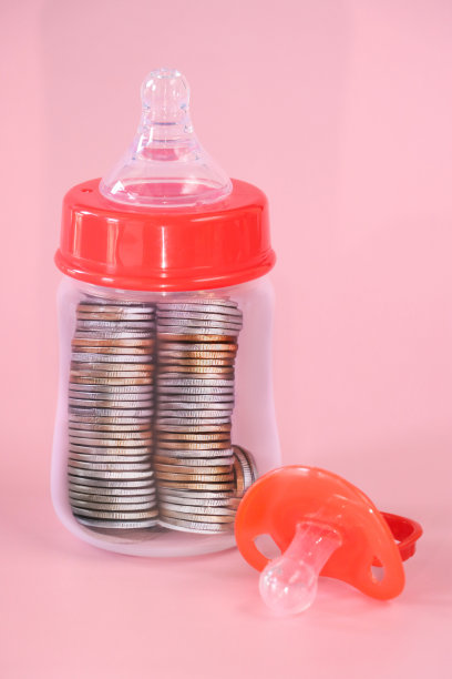 红色婴儿奶嘴(奶嘴)特写图片，塑料奶瓶配硅胶奶-头，红色瓶盖环，装满硬币的新生儿奶瓶，粉色背景，女性编码育儿，育儿成本和儿童储蓄账户概念图片下载