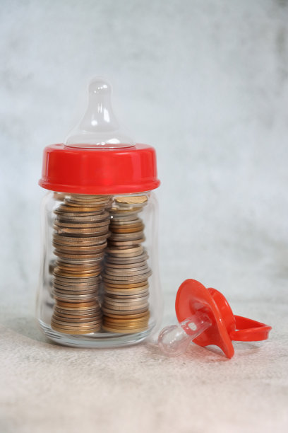 红色婴儿奶瓶(奶嘴)特写图片，塑料奶瓶配硅胶奶嘴，红色瓶盖环，装满硬币的新生儿奶瓶，斑纹灰色背景，中性编码育儿，育儿成本和儿童储蓄账户概念图片下载