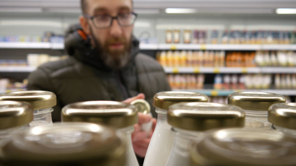 超市里许多玻璃瓶奶制品的特写镜头，一位男顾客正在挑选其中的一瓶图片下载