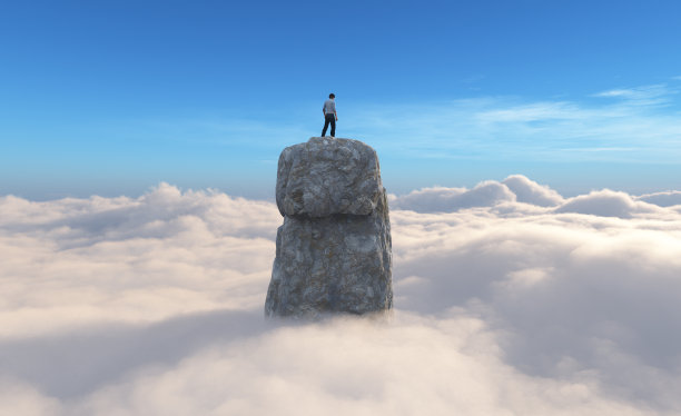 一个人站在云顶上方的岩石上。图片下载