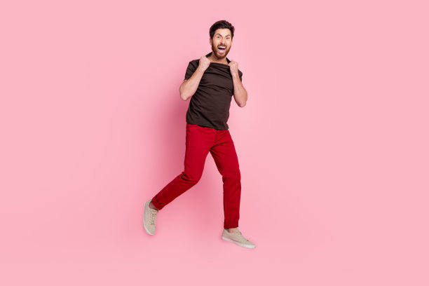 疯狂的人全身照片与鬃毛穿着棕色t恤红裤子跳撕裂衣服孤立在粉红色的背景图片下载