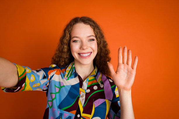 照片上的漂亮开朗的快乐女孩穿着时尚的印花衣服，手臂手掌hello hi孤立在充满活力的橙色背景图片下载