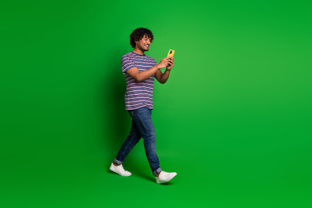 年轻的印度卷毛有趣的男子学生穿着条纹t恤去和发短信的女朋友孤立的绿色背景的肖像照片图片下载