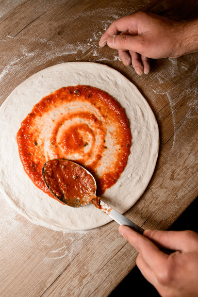Pizzaiolo将番茄酱涂在有纹理的木桌上的披萨空白上图片下载
