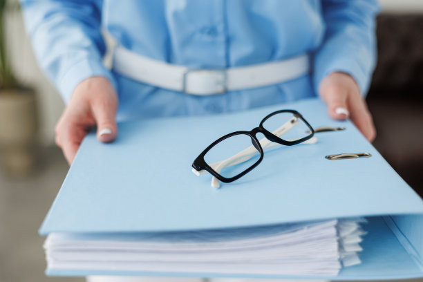裁剪后的照片中，一名身着蓝色正装衬衫、面目全非的商务女性拿着满满一叠财务文件，选择性地聚焦在眼镜上，空白的复制空间里放着广告短信图片下载