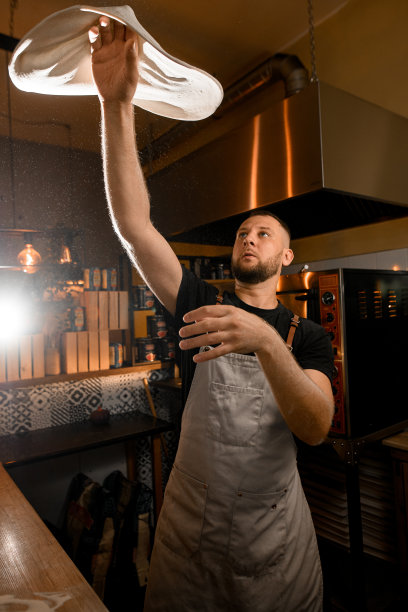 披萨师傅在厨房里用手旋转着一个圆形的披萨底座图片下载