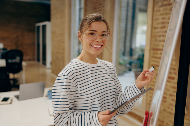 戴着眼镜微笑着的女经理在办公室的白板上写着什么，看着镜头图片下载