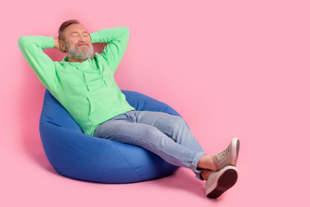 冷静的退休男子的全尺寸照片，穿着时髦的绿色衣服，在粉红色的背景上，双手放在头后睡觉图片下载