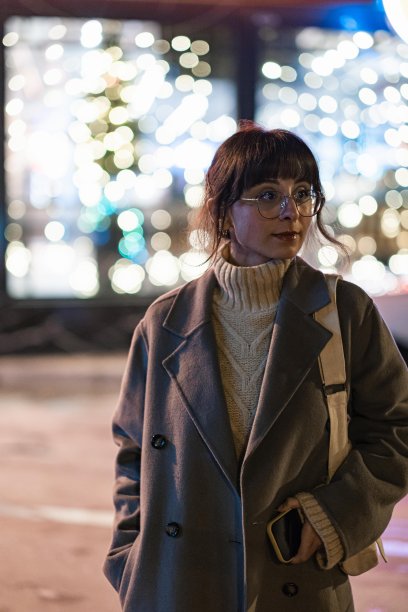 圣诞节走在街上的女人。背景中有夜晚城市灯光的散景图片下载