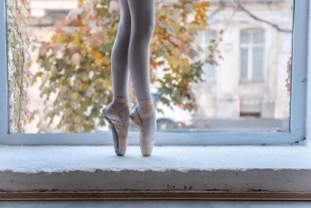 一个芭蕾舞演员的脚在窗台上的特写，与秋天的城市景观柔焦图片下载