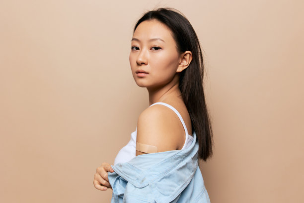 在米色粉底的背景下，晒得黝黑的可爱的年轻亚洲女士在接种疫苗后的照片。人的情绪。CoVID疫苗接种概念。复制空间报价横幅。图片下载