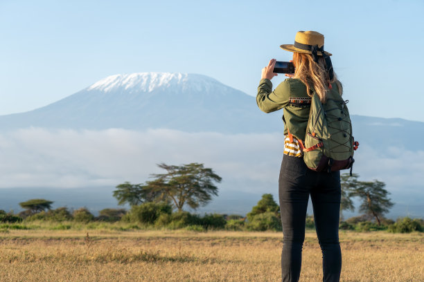 一个戴着帽子的美丽的年轻女孩站在乞力马扎罗山火山的背景下，向远处望去。旅游和非洲狩猎的概念。一位女性背包客拍摄自然和动物的照片图片下载