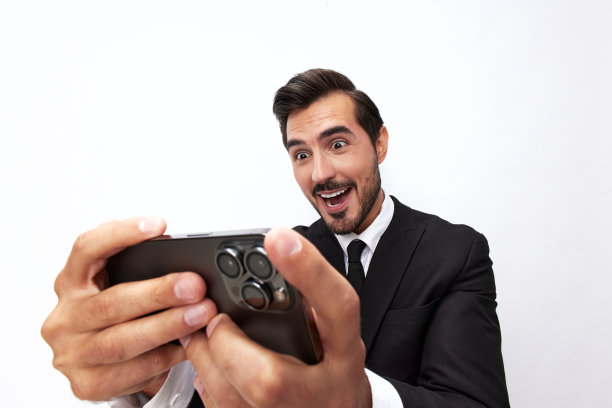 一名商人手里拿着手机，看着屏幕上的视频通话和自拍，咧嘴笑着。特写广角照片灰色孤立背景图片下载