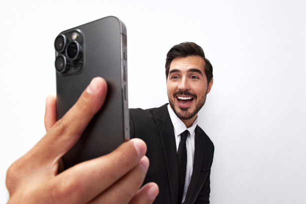 一名商人手里拿着手机，看着屏幕上的视频通话和自拍，咧嘴笑着。特写广角照片灰色孤立背景图片下载